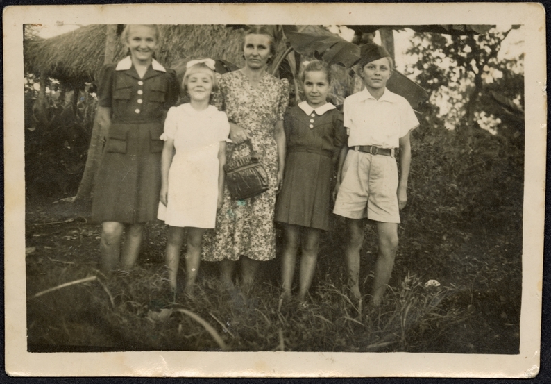 Fotografia przedstawiająca rodzinę Grójców (matkę i cztery córki), w tle wiata ze słomianym dachem. Na odwrocie dedykacja napisana odręcznie w kolorze czarnym: Na pamiątkę ofiaruje nasze rodzinne zdjęcie w dowód przyjaźni i sąsiedztwa w Afryce dla Mącewiczów od Grójców. Afryka 15/ VI 1947 r.